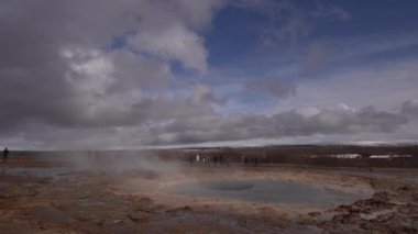 İzlanda 'nın güneybatısındaki Gayzer Vadisi. Meşhur turist eğlencesi Gaysir. Jeotermal bölge Haukadalur. Turistler, Laugarfjall tepesinin yamaçlarındaki Strokkur gayzerinin patlamasına bakıyorlar..