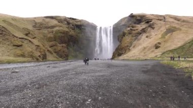 Skogafoss Şelalesi İzlanda 'nın güneyinde, altın yüzüğün üzerinde. Şelaleyi görmeye gelen ziyaretçiler, dağların eteklerinde yürüyen turistler..