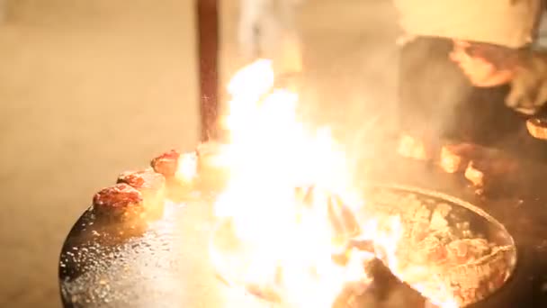 O chef derrama azeite nos bifes assados. Bife de carne está sendo preparado em uma grade ao ar livre de ferro de aço redondo com uma placa de cozinhar e uma fogueira aberta no meio . — Vídeo de Stock