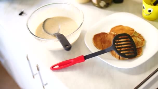 Una ciotola di pancake mix, un piatto di pancake pronti e una spatola, tre pezzi in una padella su un fornello . — Video Stock