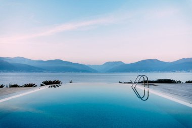 Akşam gökyüzünün yansıması deniz kenarındaki havuzun yumuşak suyunda, dağların arka planında..