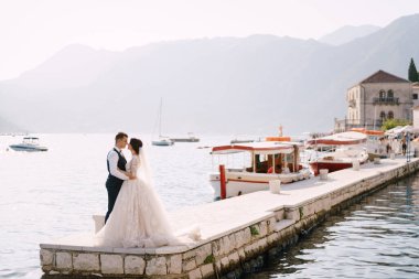 Tekne rıhtımında, dağ manzaralı ve gün batımında evlenen çift. Karadağ 'da sanat eseri bir düğün fotoğrafı, Perast..