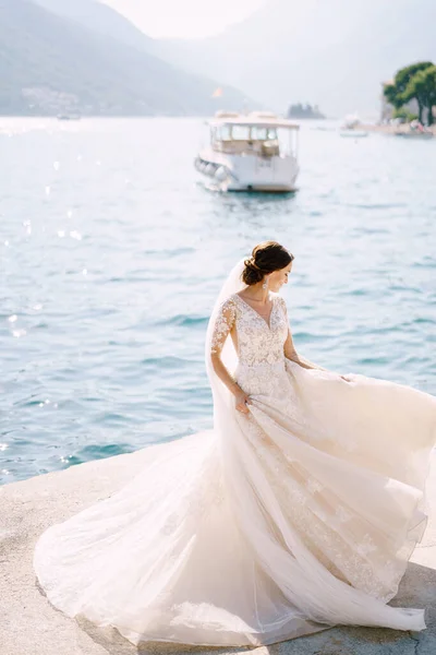 Bruden i bröllopsklänning dansar på piren och viftar med en klänning. Fine-art bröllop foto i Montenegro, Perast. — Stockfoto