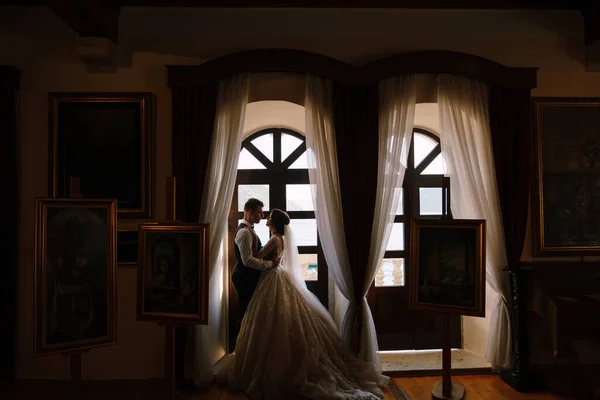 Foto pernikahan seni rupa di Montenegro, Perast. Pasangan suami-istri berdiri di dekat jendela kayu dan memeluk. — Stok Foto