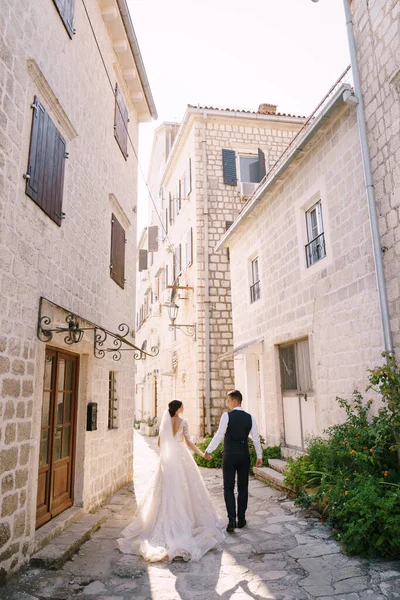 A menyasszony és a vőlegény az utcán sétálnak a régi házak között. Képzőművészeti esküvői fotó Montenegróban, Perast. — Stock Fotó