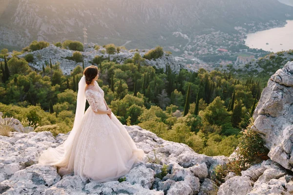 Pengantin wanita berdiri di atas gunung dengan pemandangan panorama Teluk Kotor, saat matahari terbenam. Foto pernikahan yang indah di Montenegro, Gunung Lovchen. — Stok Foto