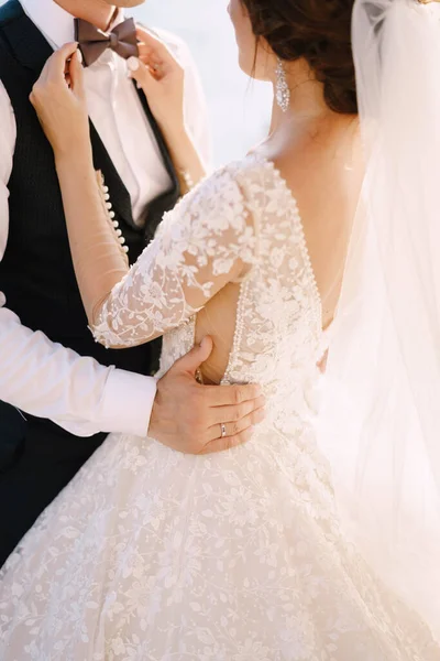 Eine Nahaufnahme der Hände einer Braut. Er spielt mit den Fingern mit einer Fliege des Bräutigams. Der Bräutigam umarmt die Braut in der Taille. — Stockfoto