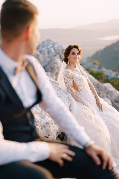 Um casal de casamentos no topo de uma montanha na Baía de Kotor, a noiva sorri para o noivo ao pôr do sol. Fotos de casamento de destino de arte em Montenegro, Monte Lovchen . — Fotografia de Stock
