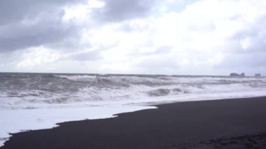 Bulutlu gökyüzü, Atlantik Okyanusu dalgaları ve İzlanda, Vik sahilinde siyah kum.