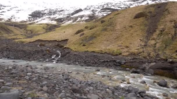 Rio de montanha pouco raso, flui de montanhas cobertas de neve para o desfiladeiro, em uma cascata de cachoeiras. Superfície montanhosa coberta de neve e pé em grama seca amarela . — Vídeo de Stock