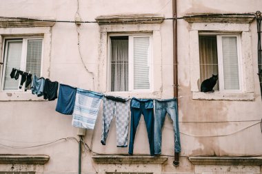 Pencerede siyah bir kedi oturuyor. Giysiler, pencereler arasındaki çamaşır ipinde kurumuş..
