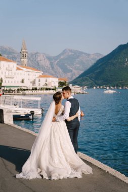 Gelin ve damat yol boyunca yürür ve Perast şehrine bakarak öpüşürler. Karadağ 'da sanat eseri bir düğün fotoğrafı, Perast.. 