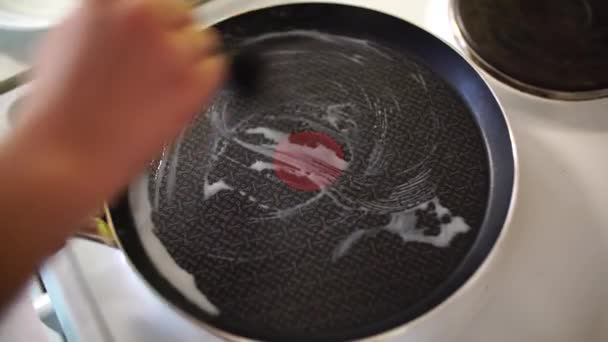Un primer plano de las manos de las mujeres untando mantequilla, en una bandeja de tortitas de teflón, sobre el fondo de una estufa eléctrica . — Vídeo de stock