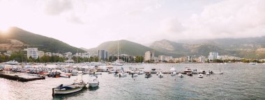 Budva seti panoraması, şehrin ve dağların zeminine karşı tekne ve yatlar için bir iskele. Güneş dağların arasından batıyor..