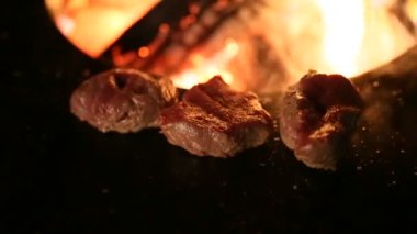 Kapalı et bifteği çelik bir ızgarada pişiriliyor. Bir tenceresi ve ortasında da ateş var..