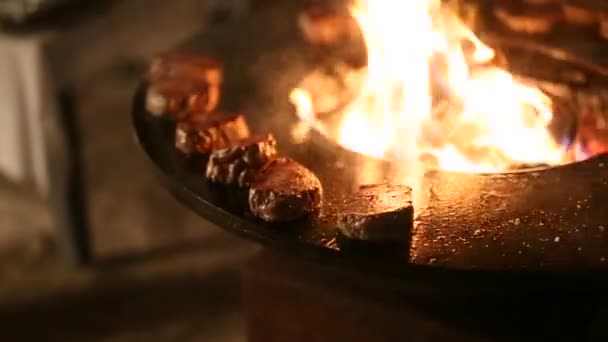 Egy közeli kép a négyzetes húsról a forró felületen. Hús steak készülnek egy kerek acél kültéri grill egy tűzhely és egy nyitott tűz közepén. — Stock videók
