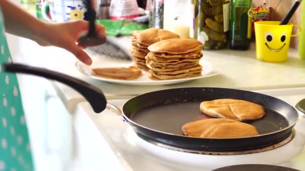 De meisjes handen in een blauw schort worden verwijderd uit de pan van de pannenkoek met een spatel. Zet de pannenkoeken in een stapel. — Stockvideo