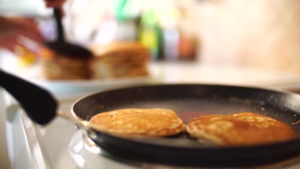 Flickornas händer i ett blått förkläde avlägsnas från pannkakans stekpanna med en spatel. Lägger pannkakorna i en hög. — Stockvideo