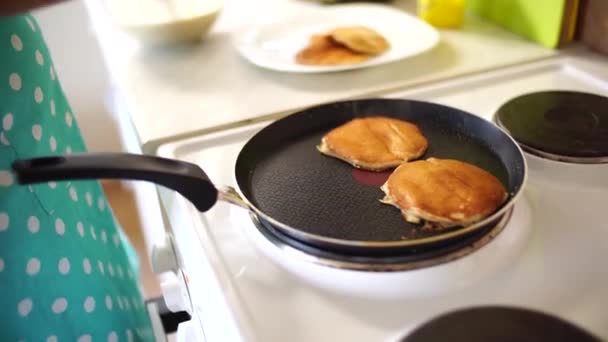 The girls hands in a blue apron are removed from the pan of the pancake with a spatula. Puts the pancakes in a pile. — Stock Video