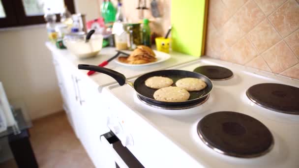 Tre pannkakor steks i en stekpanna, på en elektrisk spis, mot bakgrund av köksbordet. — Stockvideo