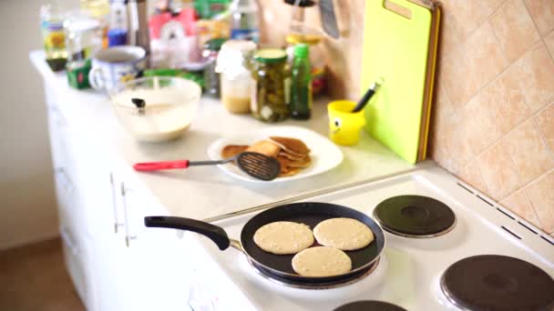 Tre pannkakor steks i en stekpanna, på en elektrisk spis, mot bakgrund av köksbordet. — Stockvideo