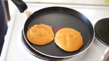 Mavi önlüklü kızlar spatulayla pankekin tavasından çekiliyorlar. Krepleri yığının içine koyar..