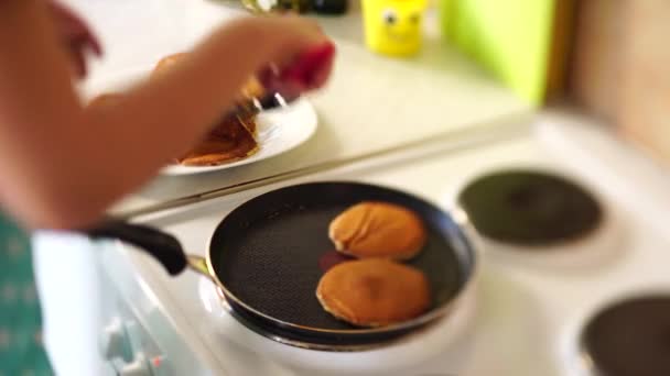 Flickornas händer i ett blått förkläde avlägsnas från pannkakans stekpanna med en spatel. Lägger pannkakorna i en hög. — Stockvideo