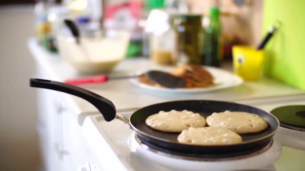 Tre pannkakor steks i en stekpanna, på en elektrisk spis, mot bakgrund av köksbordet. — Stockvideo