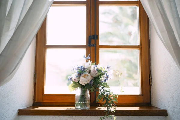 Brautstrauß aus weißen Rosen, Eukalyptuszweigen und zarten blauen Blumen in Glasvase auf der hölzernen Fensterbank — Stockfoto