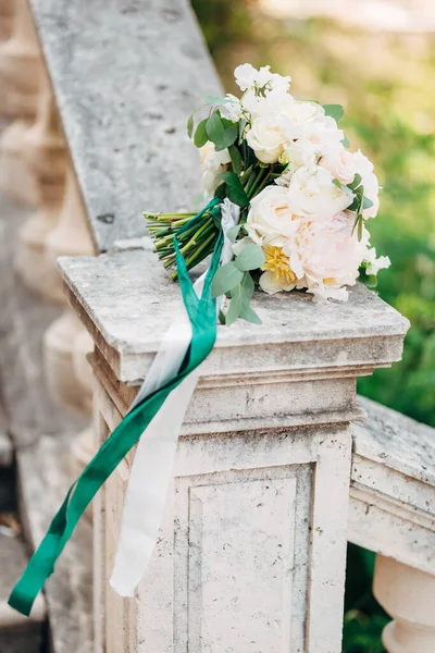 Buket pengantin putih peoni dan mawar, cabang pohon eukaliptus, dengan pita putih dan hijau di pagar tangga kuno — Stok Foto
