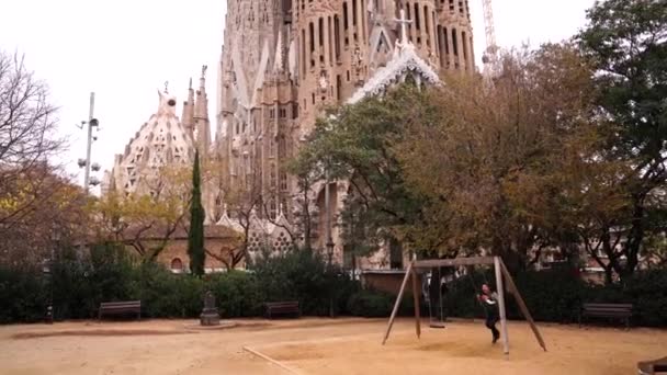 Мама с ребёнком катаются на качелях. На фоне храма Святого Семейства в Барселоне, Испания . — стоковое видео
