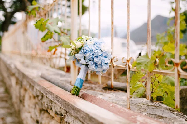 Buquê de noivas de rosas brancas, galhos de eucalipto, hortensias azuis, astros verdes e fitas azuis na cerca de tijolo — Fotografia de Stock