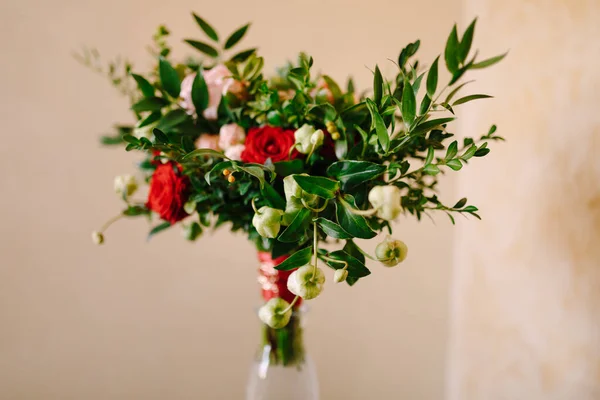 Ramo nupcial de rosas rojas y rosas, ramas de boj, brotes no florecientes de flores blancas y cintas rojas con broche en el jarrón de vidrio —  Fotos de Stock