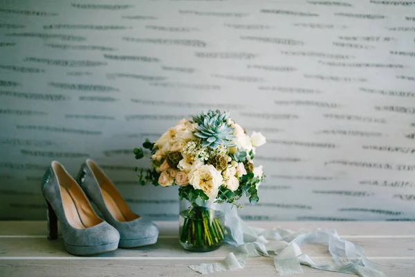 Ramo nupcial de rosas blancas, ramas de eucalipto, sempervivum, scabiosa y cintas azules en zapatos de la novia cerca de ella —  Fotos de Stock