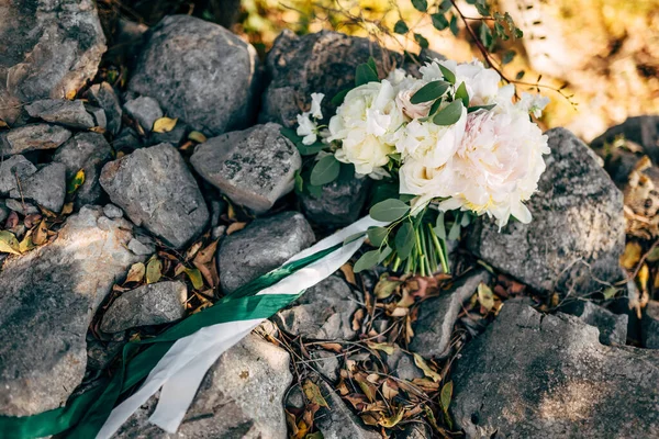 Ramo nupcial de peonías blancas y rosas, ramas de eucalipto, con cintas blancas y verdes en las piedras — Foto de Stock