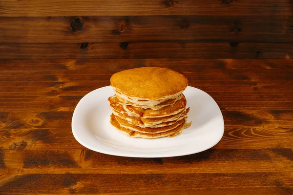 Une pile de crêpes sur une assiette, sur un fond en bois. — Photo