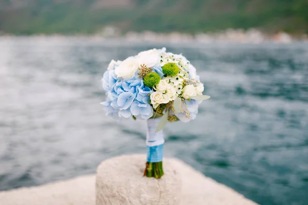 Ramo nupcial de rosas blancas, ramas de eucalipto, hortensias azules, astros verdes y cintas azules en el muelle junto al mar — Foto de Stock