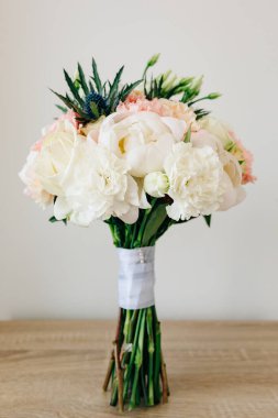 Beyaz ve pembe şakayık demeti, eryngium ve yeşil tomurcuklar, masada beyaz kurdeleler