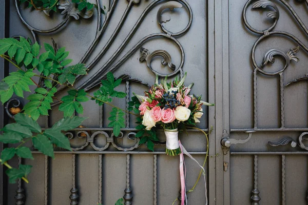 Buquê nupcial de rosas brancas e rosa, ramos de buxo, aronia, flores veronica, fitas rosa e branco na bela porta forjada — Fotografia de Stock