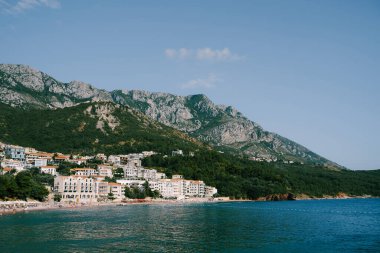 Karadağ kıyısındaki binalar ve oteller, Sveti Stefan köyündeki kayalık dağların zeminine karşı.