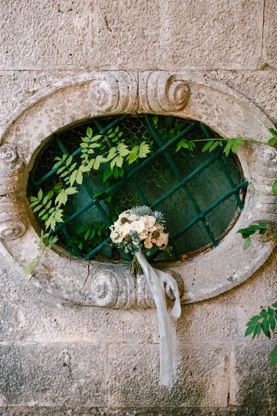 Свадебный букет белых роз, ветвей эвкалипта, полуживого, чешуйчатого и голубых лент на овальном окне старинного дома — стоковое фото