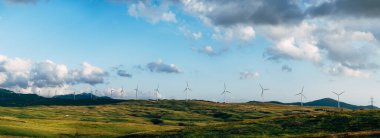 Ufukta, bulutlu mavi gökyüzü ile birlikte birçok büyük rüzgar türbinlerinin panoraması var. Yeşil teknoloji konsepti. Kuzey Karadağ 'da sanayi rüzgar çiftliği.