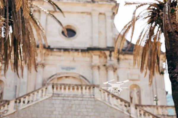 Un dron blanco vuela en el aire cerca de un templo antiguo . —  Fotos de Stock