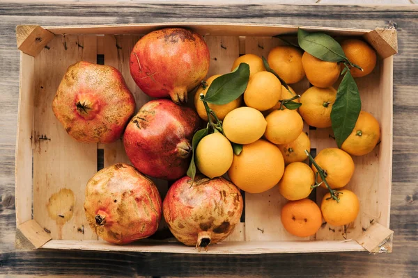 Деревянная коробка с мандаринами, лимонами и гранатами. Плоды, собранные в осеннем саду . — стоковое фото