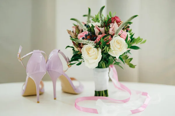 Ramo nupcial de rosas blancas y rosadas, ramas de boj, aronia, flores de verónica, cintas rosadas y blancas en la mesa y zapatos rosados de la novia —  Fotos de Stock