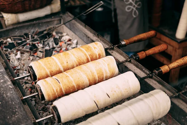 Budapeste Sweets húngaros Kurtoskalacs Chimney pastelaria cuspir bolo no mercado de Natal. Delícia sazonal tradicional de inverno com pão de leite e açúcar grelhado sobre fogo . — Fotografia de Stock