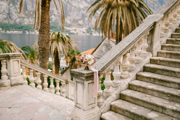 Buquê de noivas de rosas brancas e rosa, peônias, delphinium, astilbe e fitas brancas no corrimão de uma escadaria antiga com vista para a Baía Kotor — Fotografia de Stock