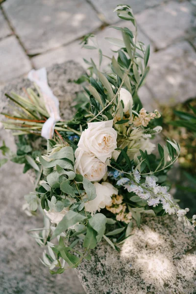 Buquê de noivas de peônias brancas e creme, rosas, veronica, delphinium, galhos de eucalipto com fita branca na cerca de pedra antiga — Fotografia de Stock