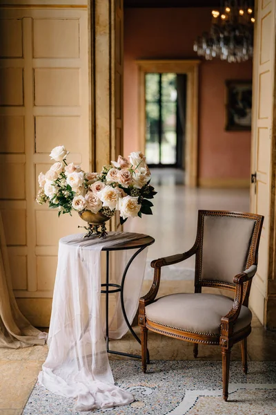 Ramo de rosas crema tierna en jarrón de cobre sobre la mesa en la elegante habitación con sillón vintage —  Fotos de Stock
