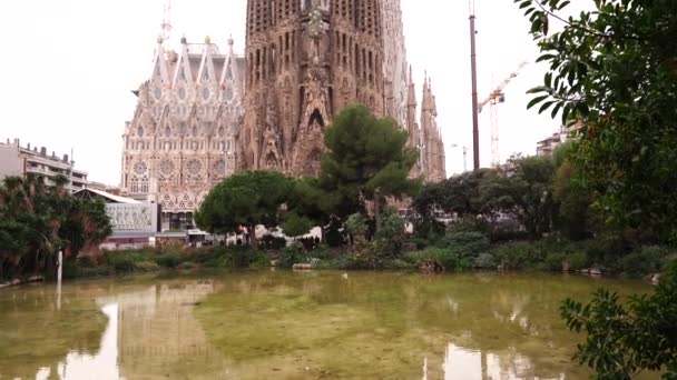 사그라다 파밀리아 (Sagrada Familia) 의 크리스마스 풍경은 공원에서 교회의 모습을 보여준다. 건축용 크레인 이 건물을 짓고 있다. — 비디오